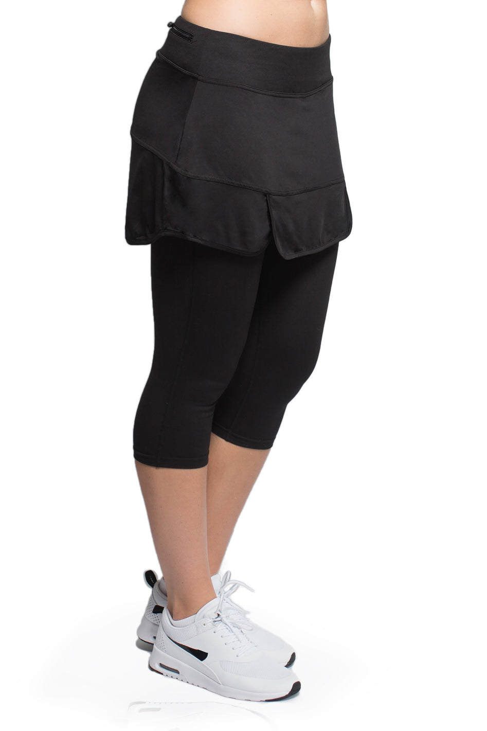 Side view of woman posing in the black version of the Endurance Skirted Capri Legging#color_black