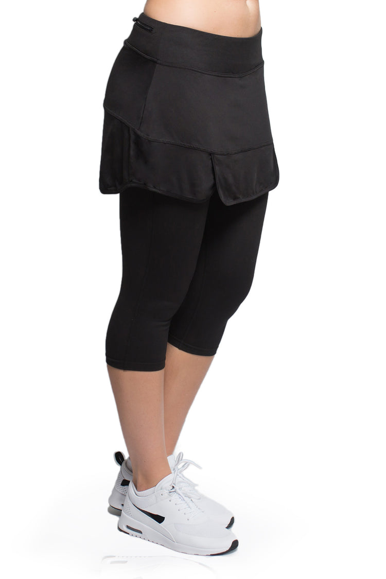 Side view of woman posing in the black version of the Endurance Skirted Capri Legging#color_black