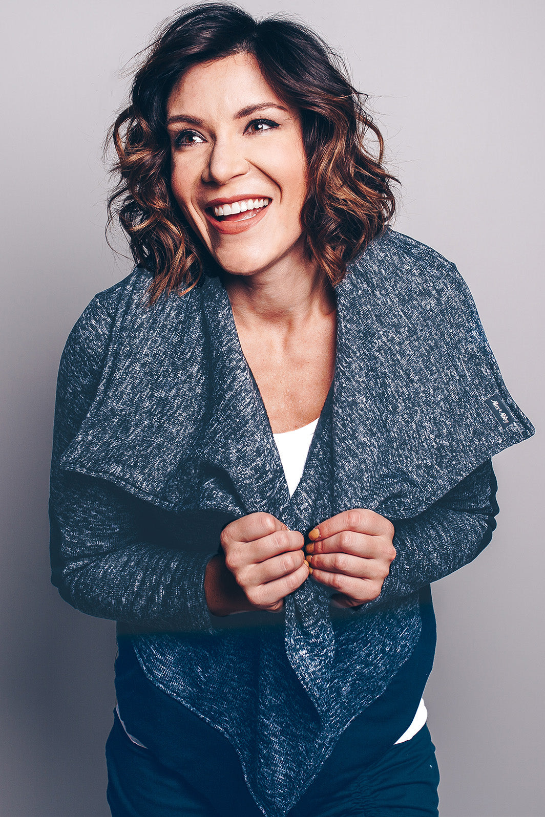 #color_black A smiling woman wearing a long-sleeve, oversized moto jacket in a gray marled pattern with a modern collar. She is also wearing a white top and blue jeans.